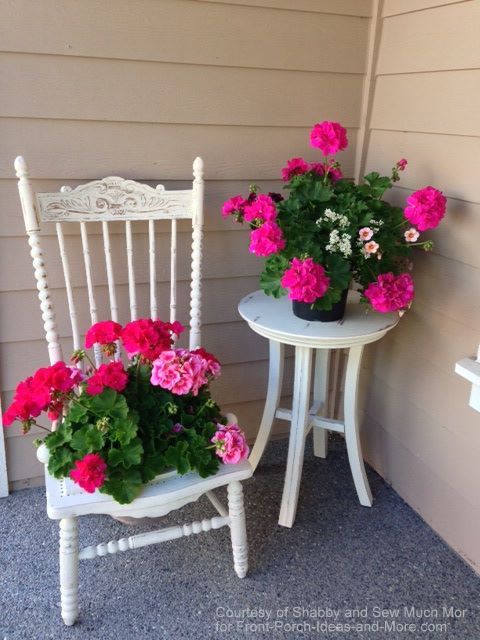 White chair and table with pink geraniums at corner of front porch