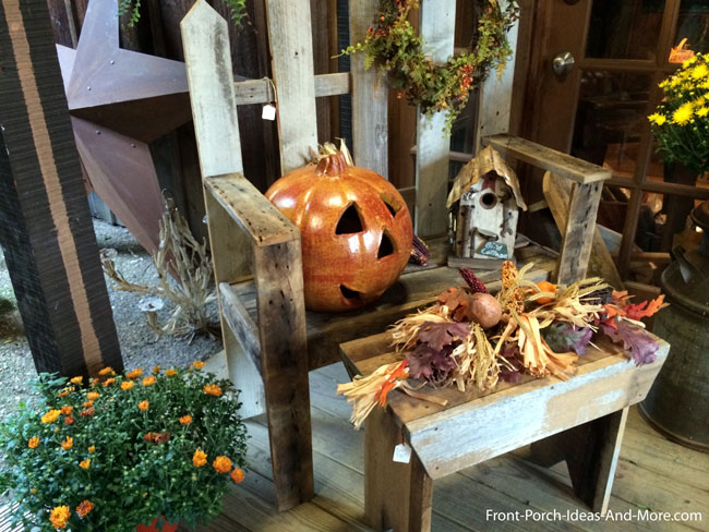 front porch decorated for fall with fence slat chair, pumpkin, and cornstalks
